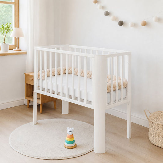 Weißes Babybett mit Matratze und beiger Zopfschlange im hellen skandinavischen Babyzimmer