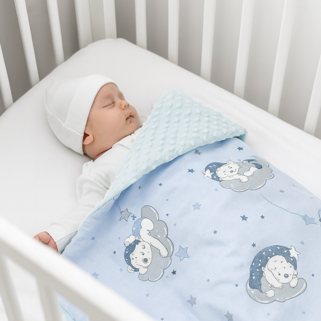 Schlafendes Neugeborenes liegt in einem weißen Babybett, trägt weiße Kleidung und Mütze, bedeckt mit einer hellblauen Babydecke mit Bärenmotiv