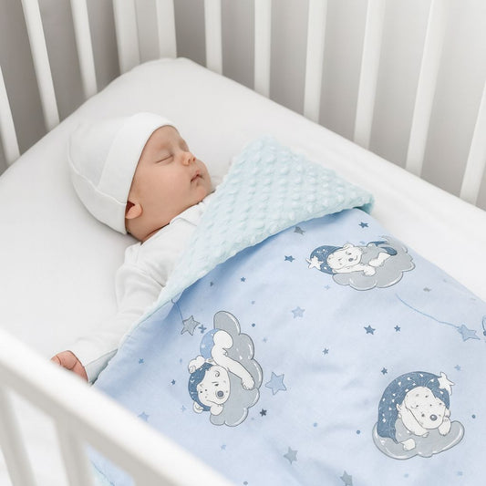 Schlafendes Neugeborenes liegt in einem weißen Babybett, trägt weiße Kleidung und Mütze, bedeckt mit einer hellblauen Babydecke mit Bärenmotiv