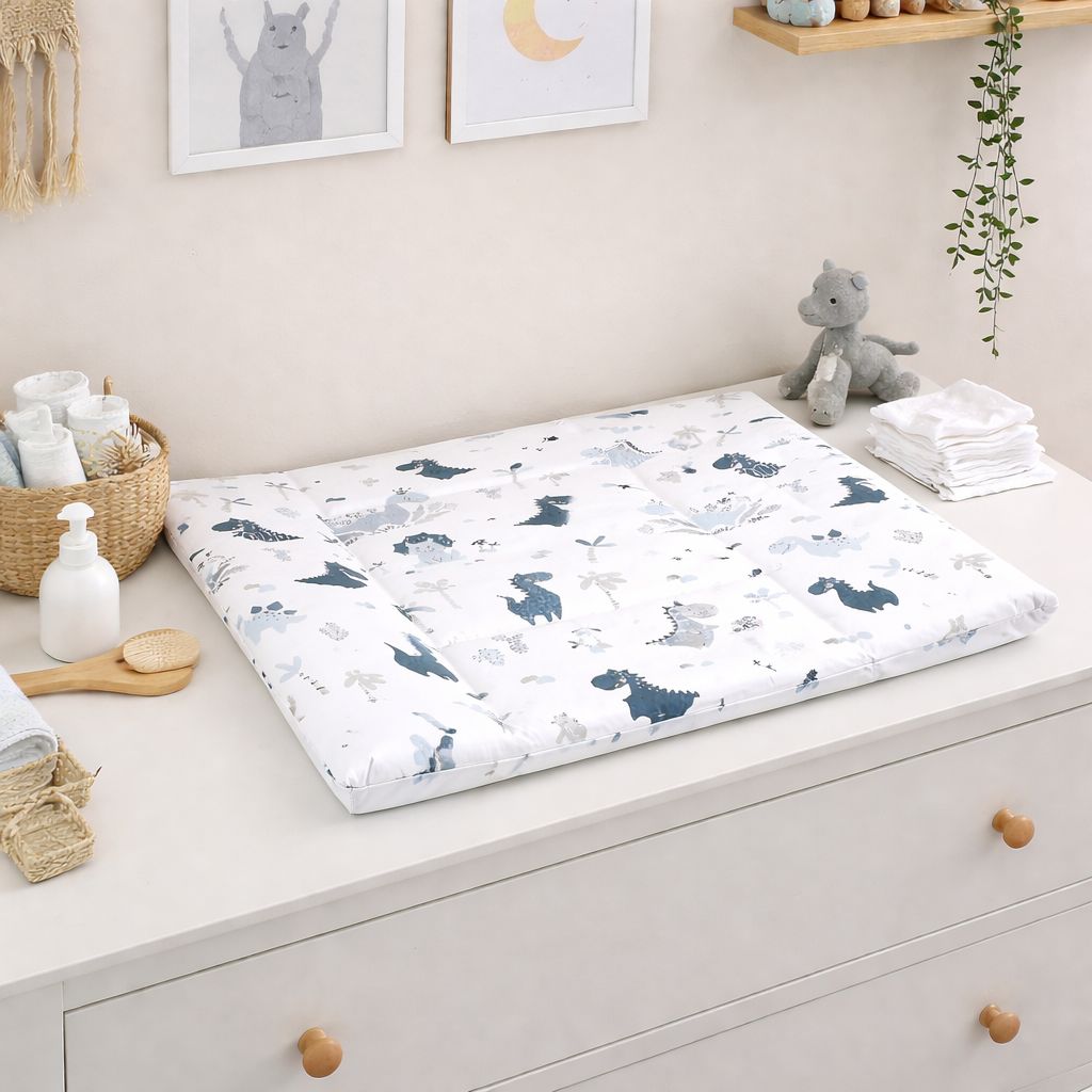 Flache Baby Wickelauflage 75 × 75 cm mit Dinosaurier-Motiven in Blau und Grau, aus Baumwolle, liegend auf weißer Wickelkommode im Kinderzimmer
