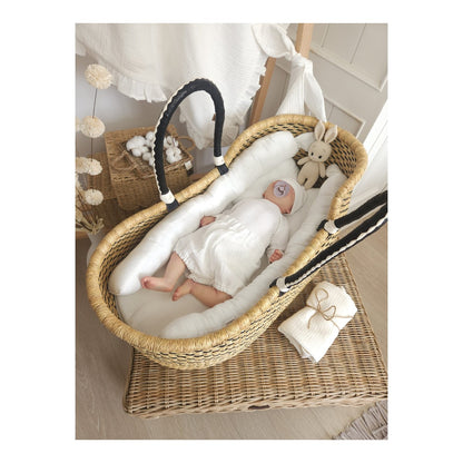 Schlafendes Baby in einer geflochtenen Wiege mit weißer Musselin-Bettwäsche und Nestchen